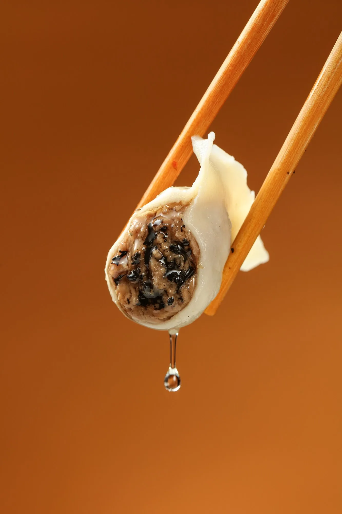 A truffle dumpling opened with chopsticks, juices running out