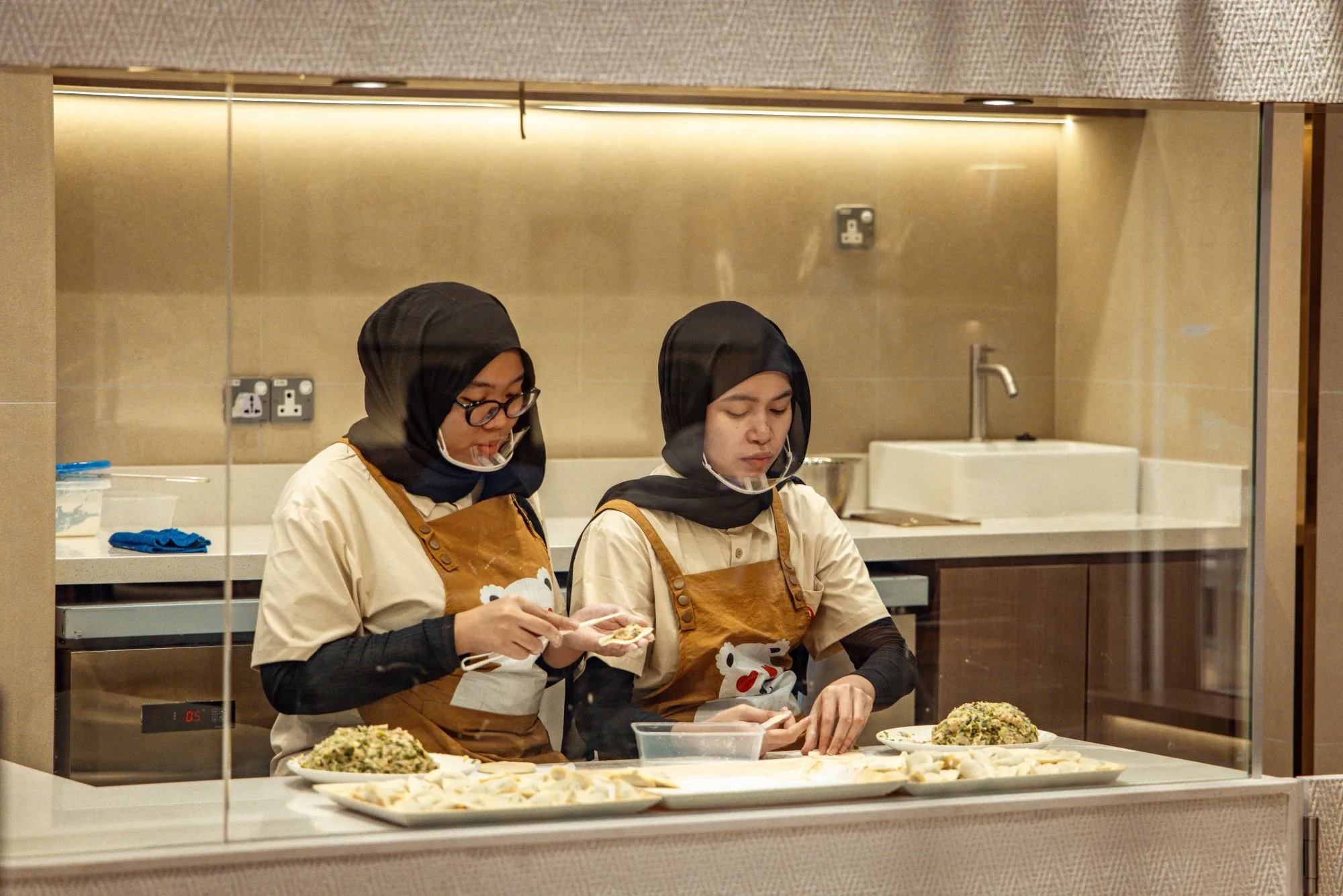 Two of our team wrapping dumplings behind the open-kitchen glass